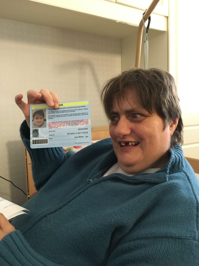 A woman holds up a Blue Badge for Disabled Parking. She looks happy with it.
