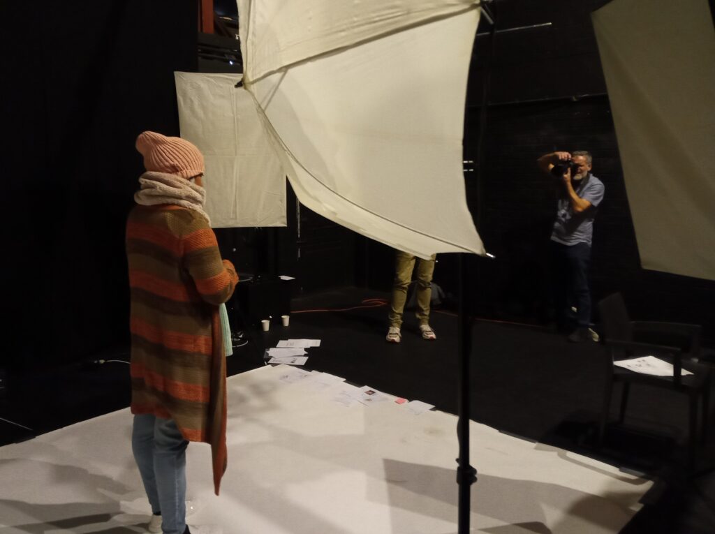 a woman stands in a photo studio with lighting equipment. A photographer is about to take her photo.
