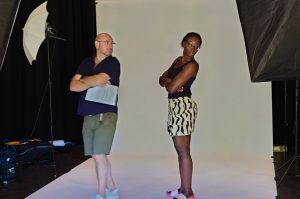 A man stands next to a woman modelling a pose he wants her to take.